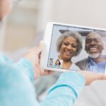 A senior couple laugh as they video chat from the screen of their unrecognizable granddaughter's digital tablet screen. She hold's the tablet with both hands.