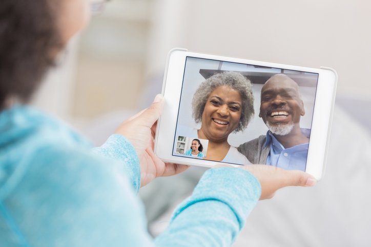 A senior couple laugh as they video chat from the screen of their unrecognizable granddaughter's digital tablet screen. She hold's the tablet with both hands.