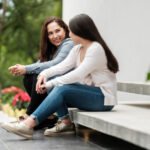 A latin mother and her teenage daughter sitting outside home and having a talk.
