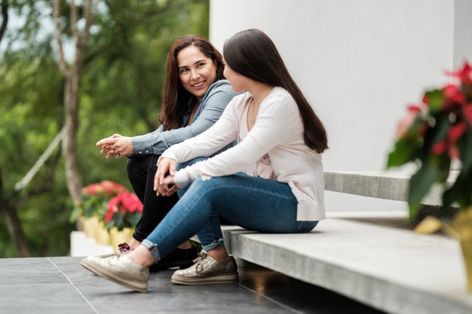 A latin mother and her teenage daughter sitting outside home and having a talk.